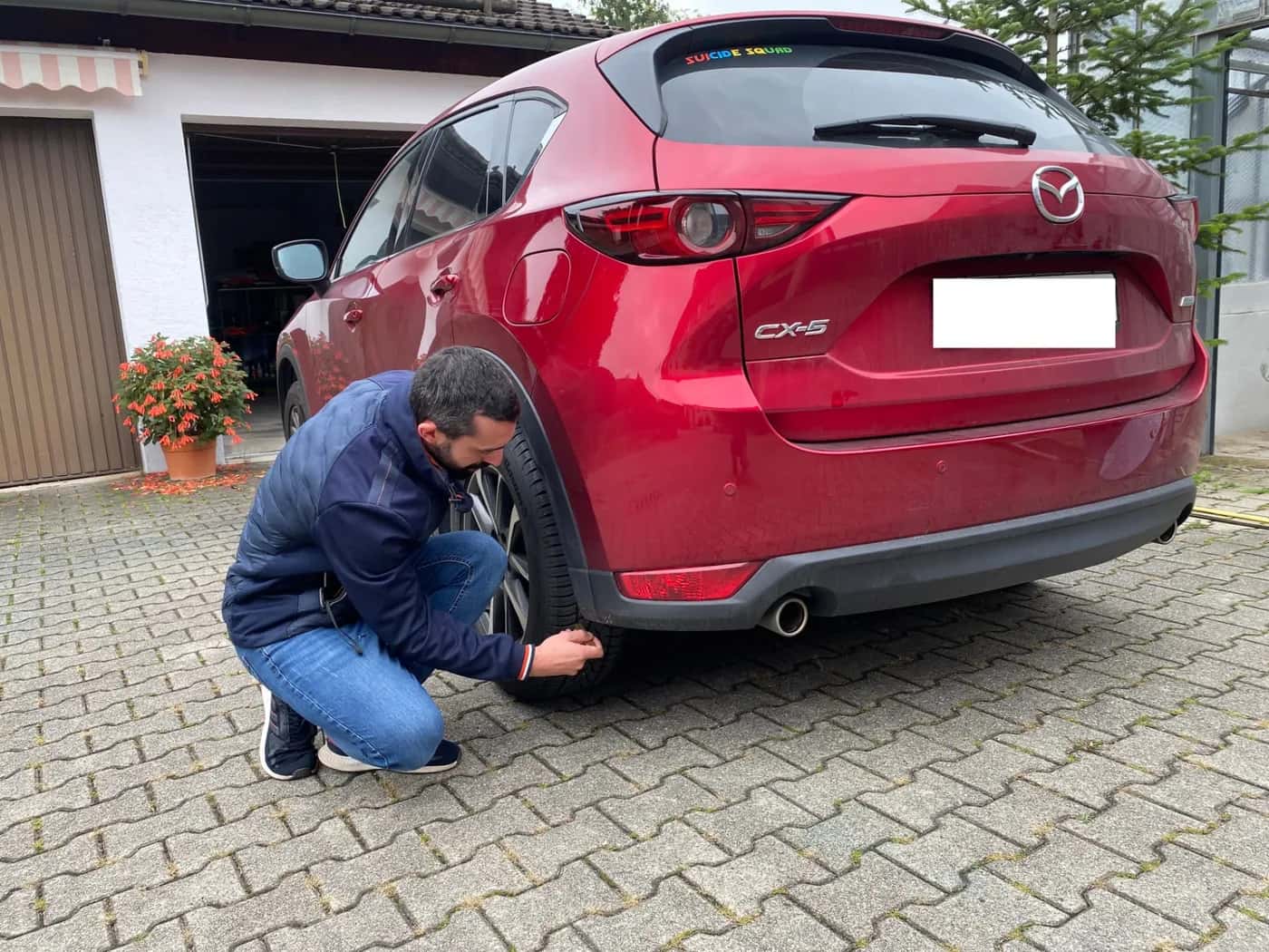 Sachverständiger untersucht den hinteren Radlauf eines roten Mazda vor einer Garage